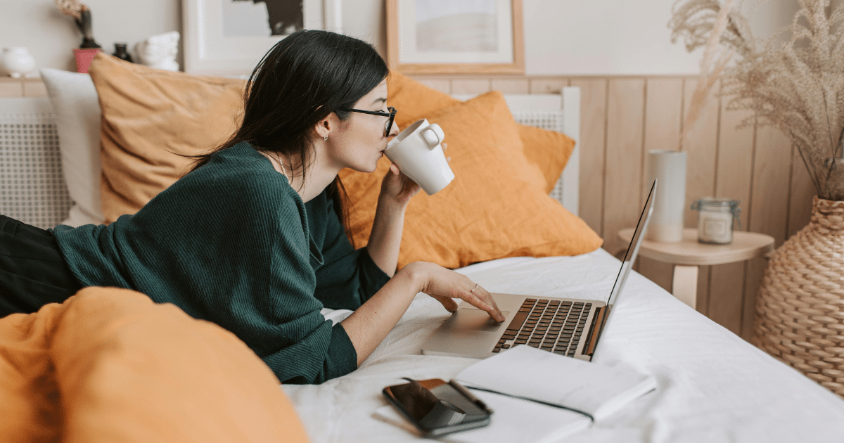 image-14 - California Mental Health Teletherapy: Woman using laptop in bed, drinking coffee. Shows modern mental health treatment and online therapy convenience.