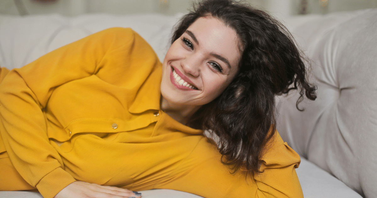image-23 - California Mental Health Smiling woman in yellow shirt lying on a couch, promoting mindfulness techniques for mental health.