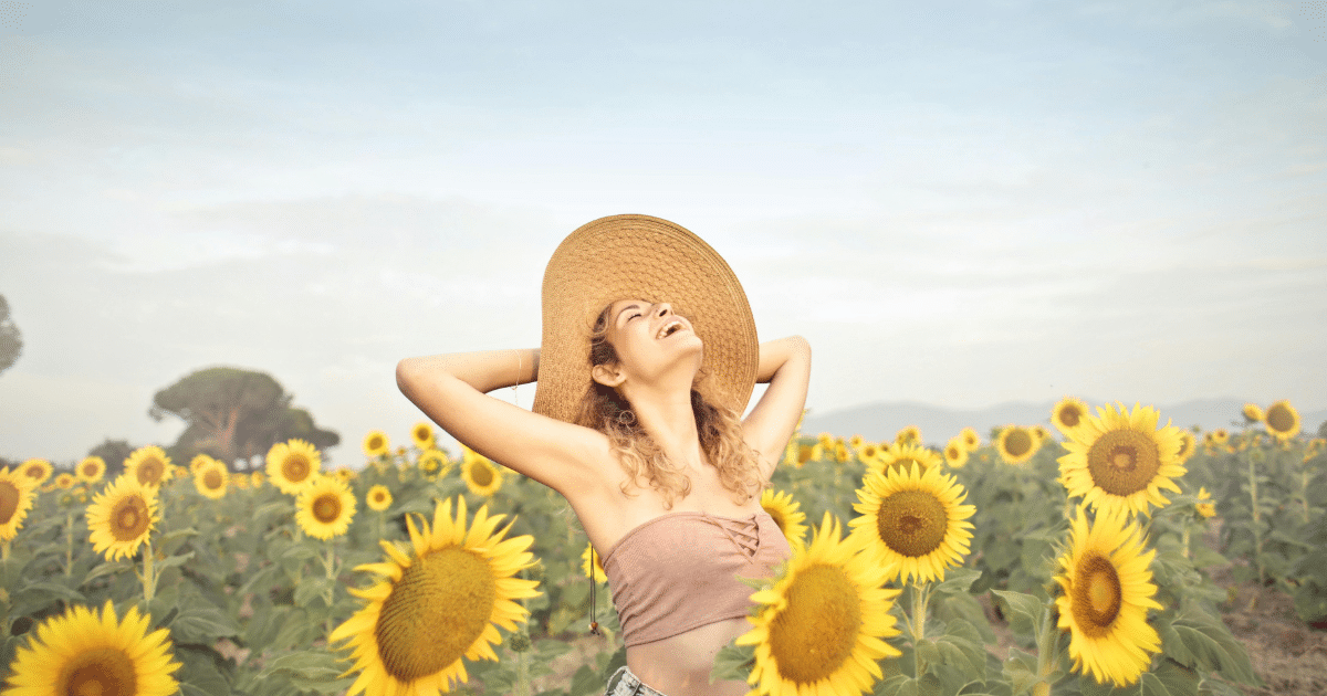image - California Mental Health Woman in sunflower field, hat, stress relief, brain health. Smiling, enjoying nature, reducing long-term stress impact.