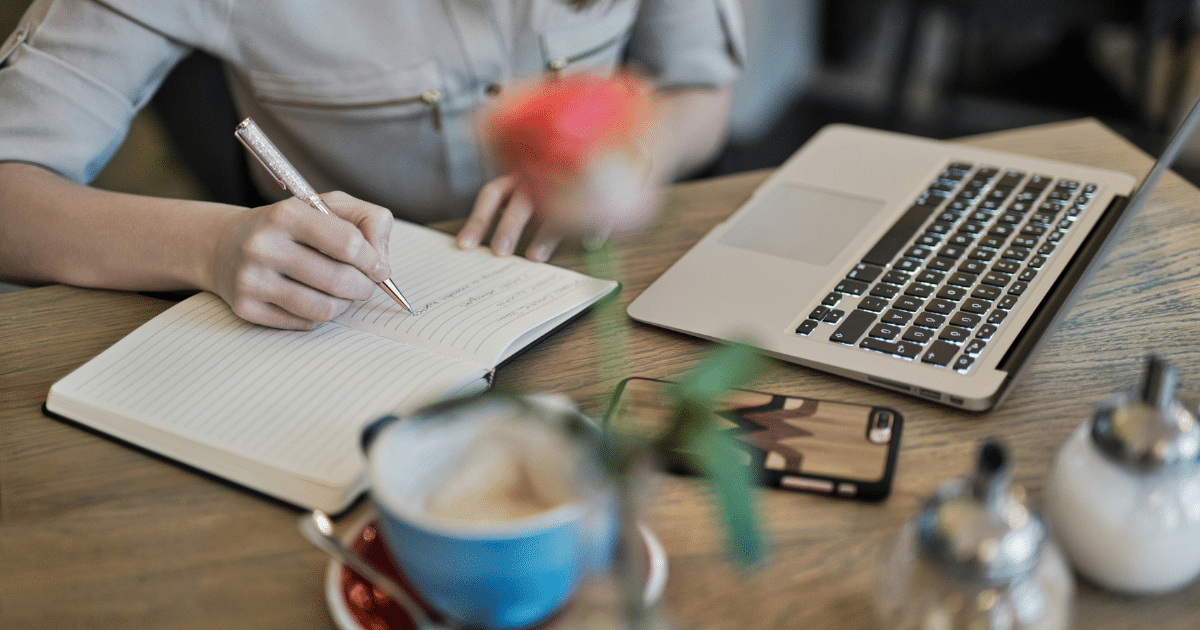 image - California Mental Health Journaling for mental health: Woman writing in notebook with laptop and coffee nearby. Benefits of daily journaling.