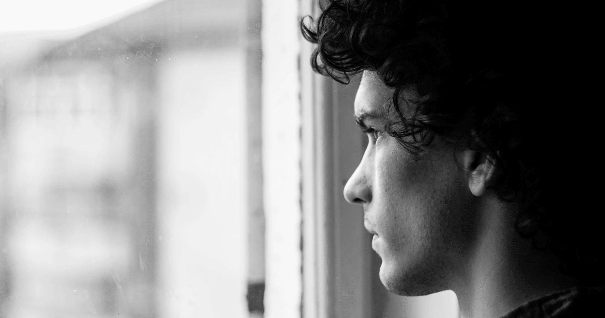 AD_4nXcDsbW7esFn68clP0-dCDcKpTvk6vYhNftp4-lw_MQWVK59rPoCtFZffRNR0afXHmS--qSLhiBB4PLkQiY9OrvJfhwc7duV35Ck0_DQq10sqv-KEJYG8y8roWtdcloxUtAcJe0GIw - California Mental Health Monochrome image of a man looking out the window, representing OCD and paranoia's impact on mental health.