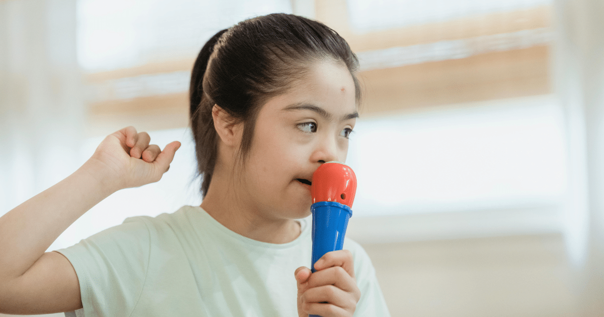 AD_4nXfjA5b7J4pbFXrDuM7WiT06-jL0YbxwJvLOi8WVm_99GsWfVauSkv4fIy0Ijt2ccnCoORVh081ketaCrluSln-DxZvW4YJ-PUlstkcfZqEum1HA-9zqOhk1j_ZGcUMRIfyYF_4PKg - California Mental Health Young woman with Down syndrome singing into a toy microphone, illustrating autism signs in women.