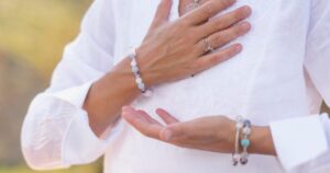 - California Mental Health Close-up of a person in a white tunic with hands crossed over the chest, wearing beaded bracelets and rings.