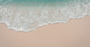 - California Mental Health Aerial view of turquoise waves washing onto a smooth sandy beach with white foam arriving at the shore, calm seaside scene.