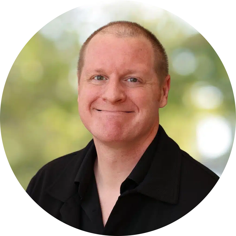 image-17webp - California Mental Health Smiling man in a black shirt outdoors, blurred green background behind him.