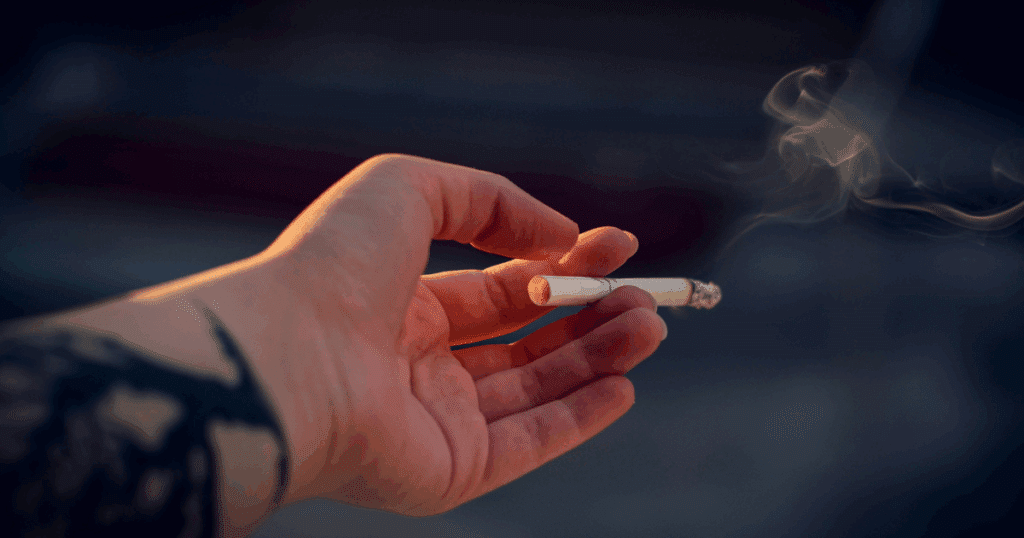 Hand holding a lit cigarette with smoke, illustrating the link between nicotine and anxiety.