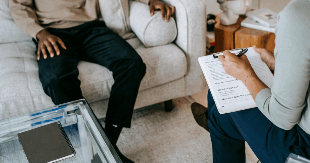 Therapy session: Therapist taking notes while patient sits on couch. Mental health support and counseling concept.
