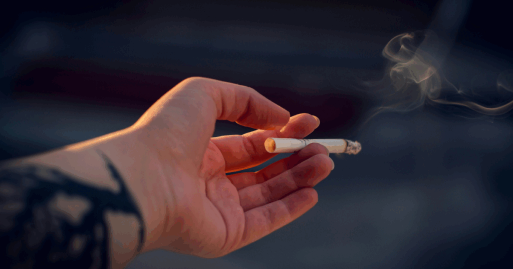 Hand holds a lit cigarette with smoke, illustrating the link between nicotine and anxiety. Addiction concept.