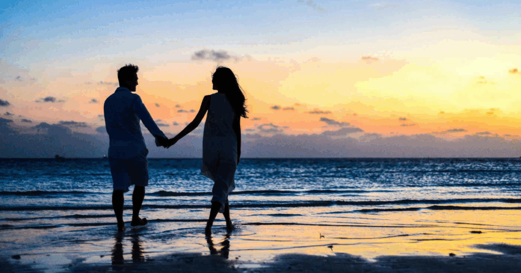 Couple holding hands at sunset beach. Intimacy and mental wellbeing concept for anxiety relief through sex and relationships.