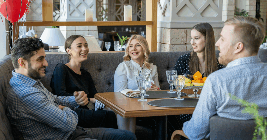 Group of friends smiling and laughing together at a restaurant, enjoying their time. Social gathering, friends, restaurant.