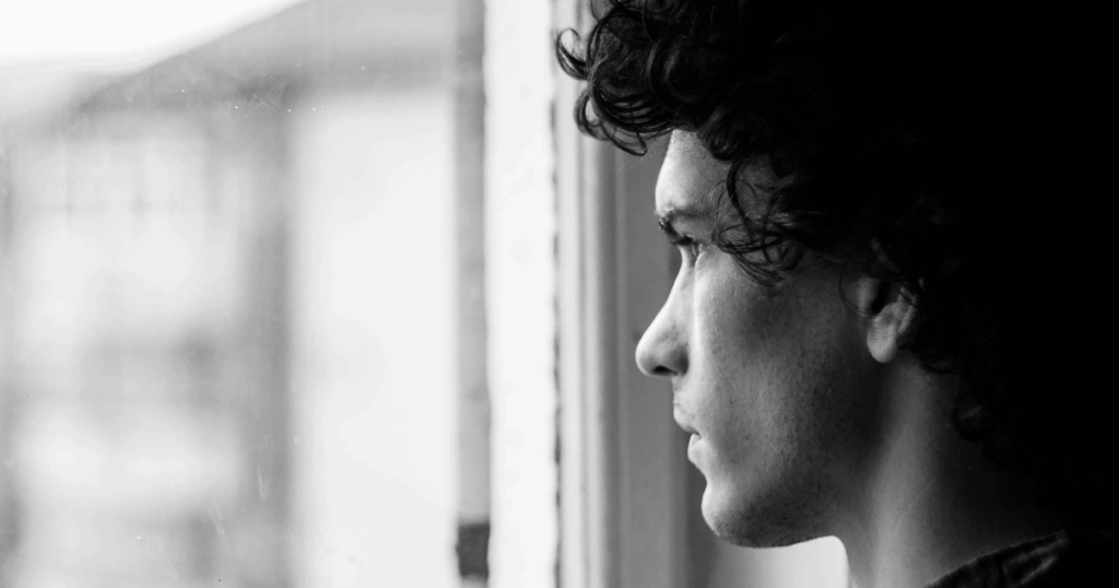 Black and white portrait of a thoughtful young man looking out the window. Mental health and elimination disorders concept.