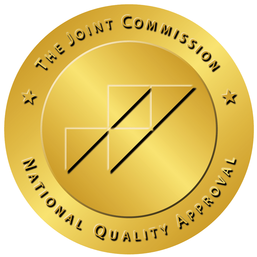 Gold circular accreditation seal reading 'The Joint Commission National Quality Approved' with a central geometric emblem in gold